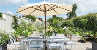 Summer garden with a dining table covered with a parasol to provide garden shade