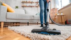 woman vacuuming rug in living room to support an expert opinion to answer 'why does my room smell when I vacuum'