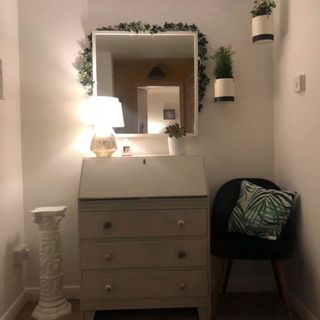 hall way with white wall and square wall mirror and a white drawer with table lamp