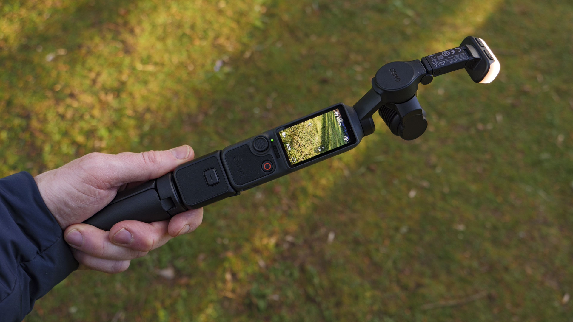 DJI Osmo Pocket 4 vlogging camera in the hand with battery grip, mini tripod and fill light attached