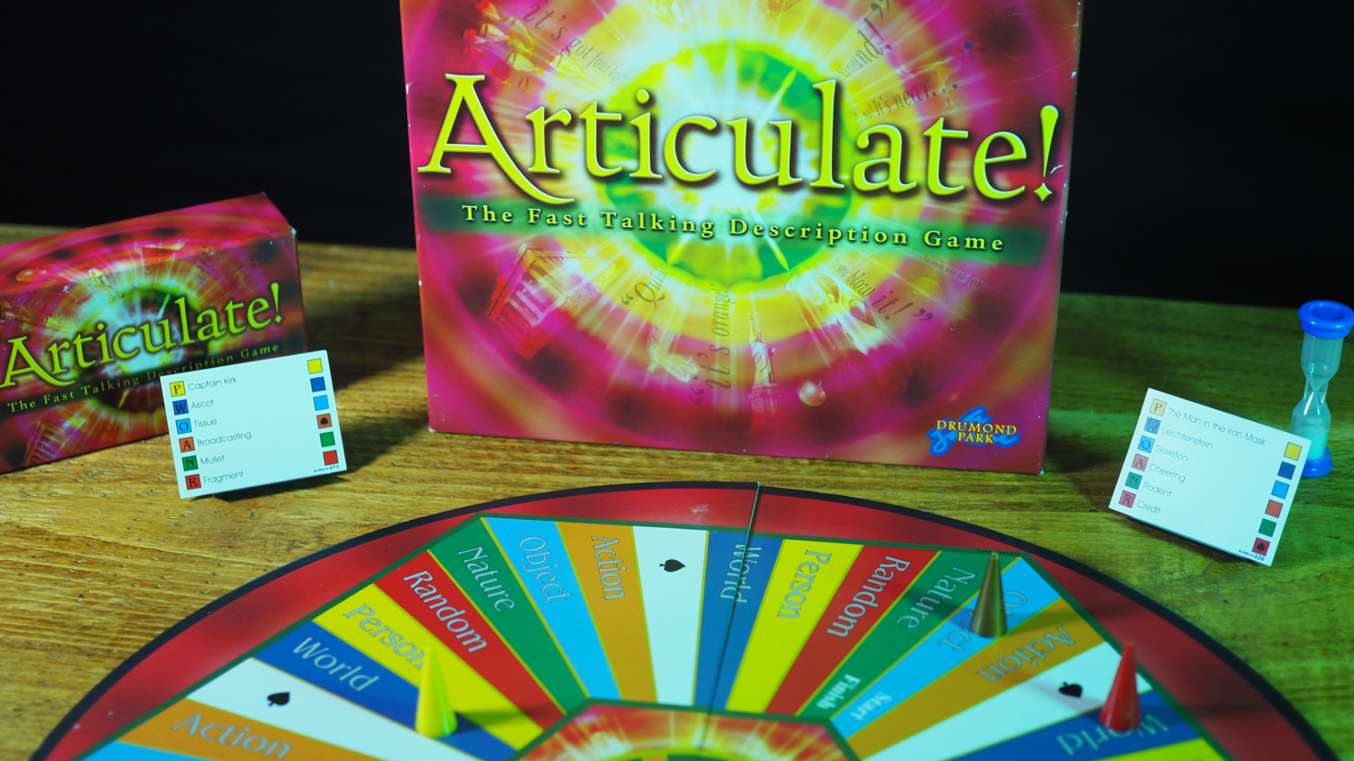 Articulate box, cards, and board on a wooden table, against a black background