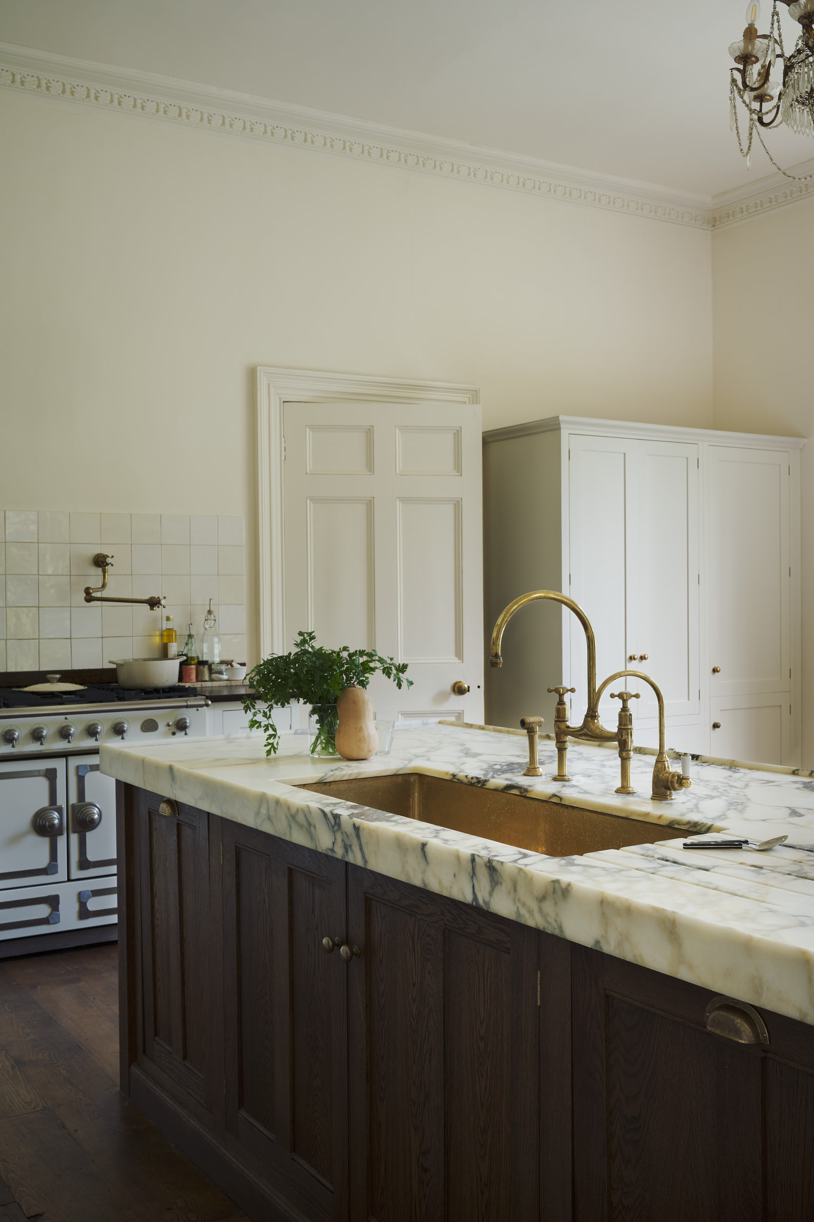 A classic English kitchen with a heavily-veined marble countertop and brass taps and sink