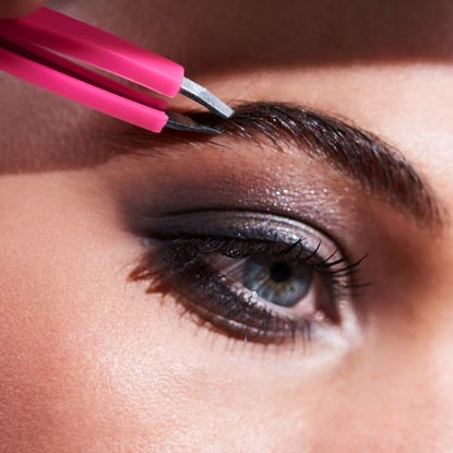 woman plucking her eyebrows with tweezers
