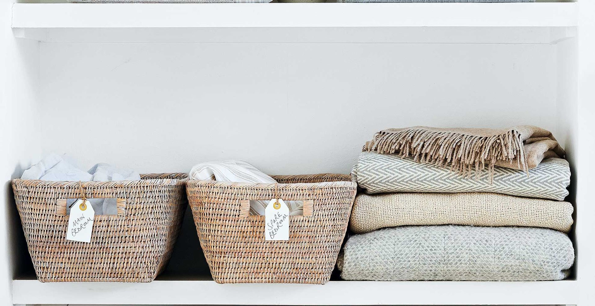 White shelf with labeled baskets and piled blankets to show decluttering as a spring cleaning mistake to avoid
