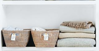 White shelf with labeled baskets and piled blankets to show decluttering as a spring cleaning mistake to avoid