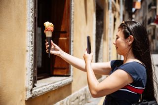 girl holds icecream and takes a photo in the street