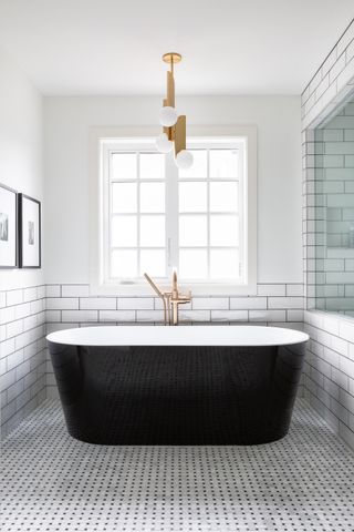 A bathroom with white walls and a black bathtub, and gold accessories