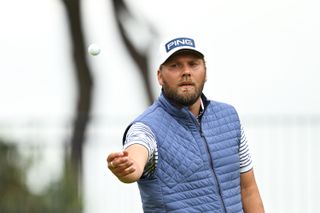 Daniel Brown throws a golf ball to his caddie