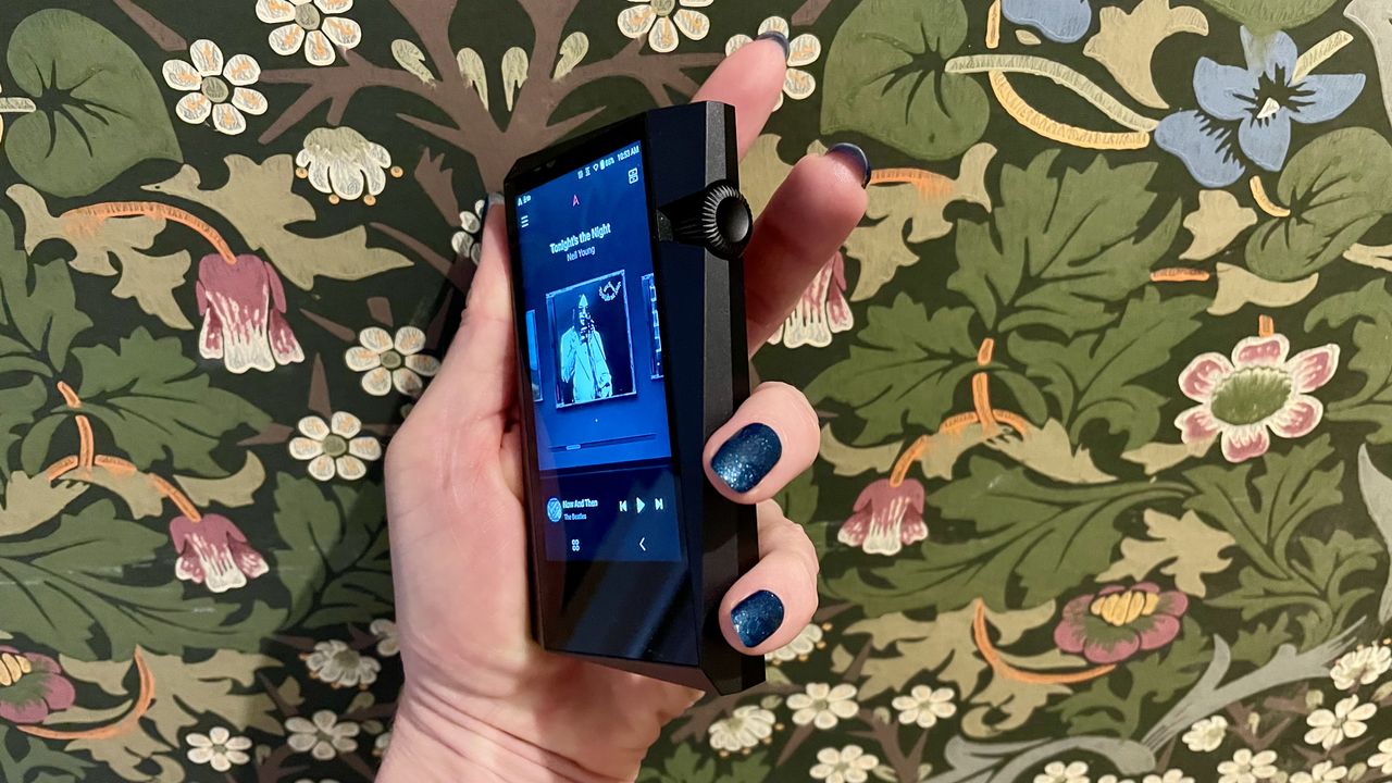 Astell &amp; Kern A&amp;norma SR35 held in a ahnd to show off the rotary volume dial, on colorful background