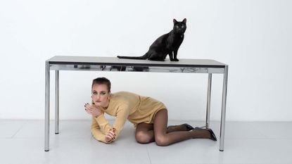 Woman in best of S/S 2023 Raf Simons under desk with black cat on it