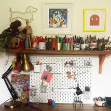 Teenage boy bedroom desk topped with open shelf filled with pens and pencils, below with framed artwork and neon light