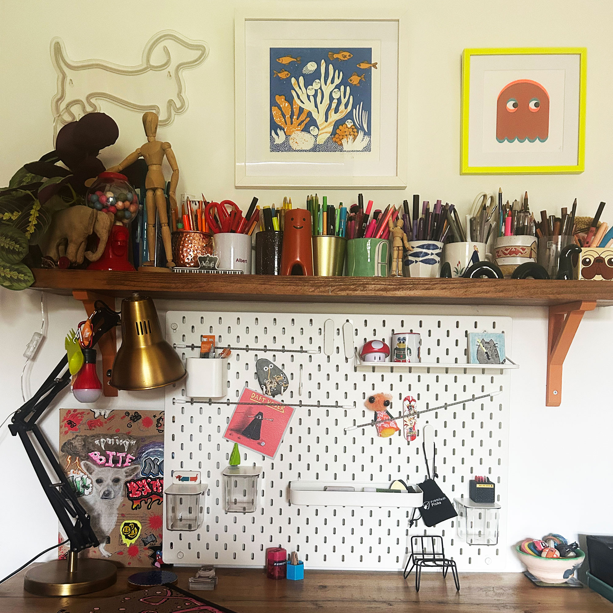 Teenage boy bedroom desk topped with open shelf filled with pens and pencils, below with framed artwork and neon light