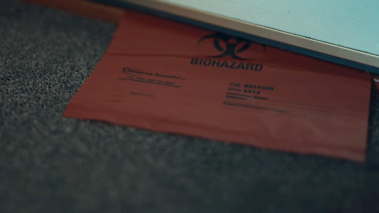 A red biohazard bag being slid under a door in Trainwreck: Poop Cruise