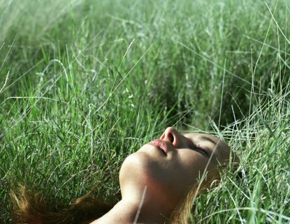 A woman lying in the grass trying meditation for slepe