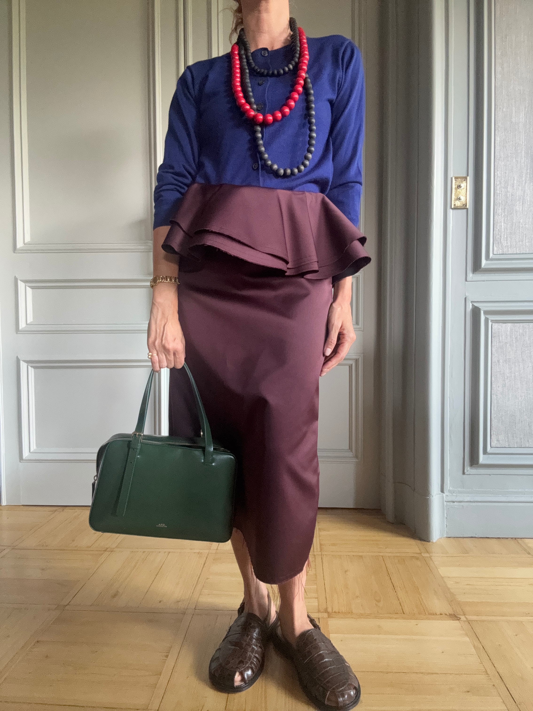 blanca miro wears a navy jumper, purple skirt and brown loafers with a green handbag