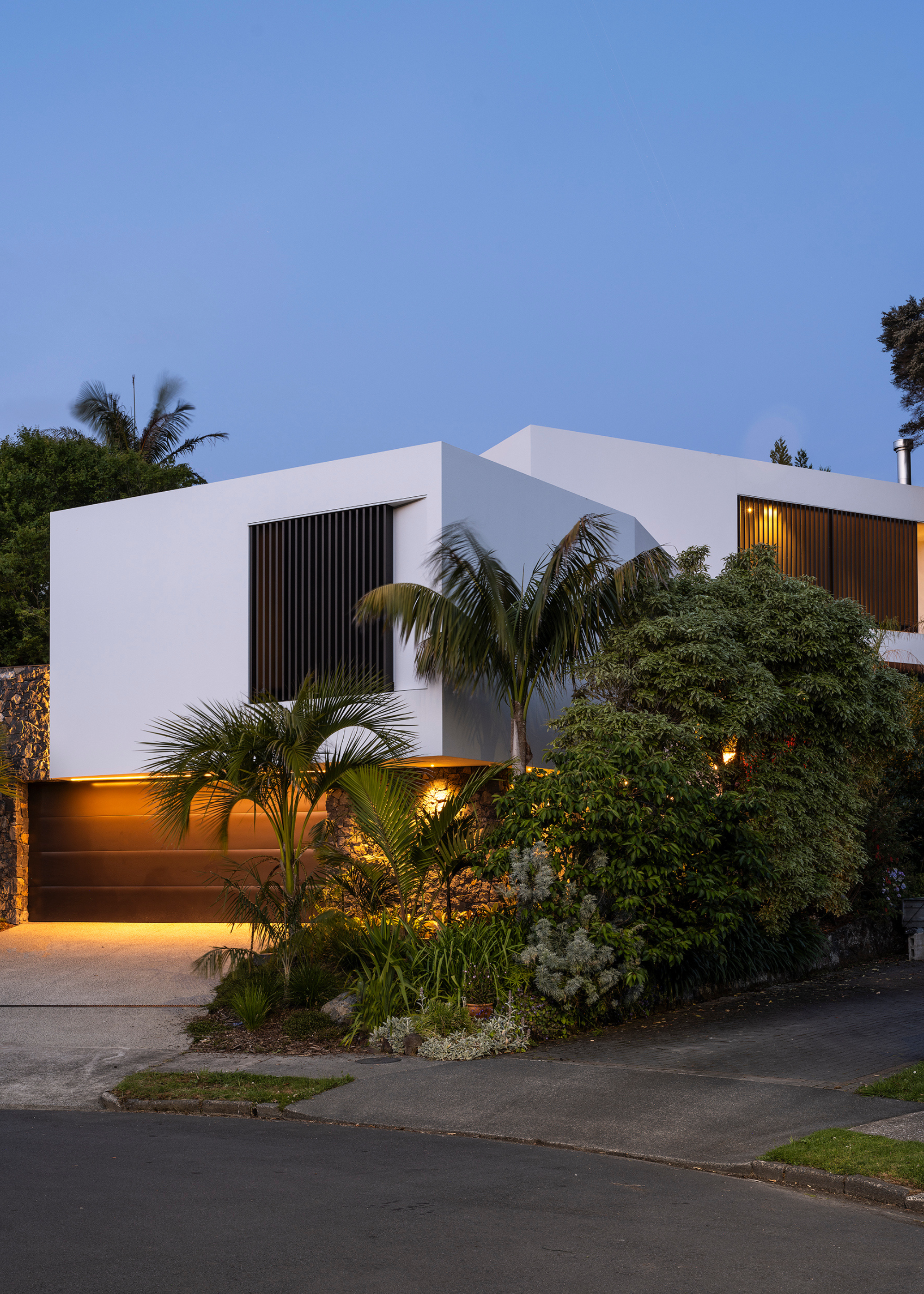 a modern white home with smart hidden lighting is surrounded by palm trees and other plants