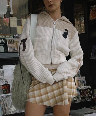 @alyssainthecity in a cream sweater plaid skirt and furry bag