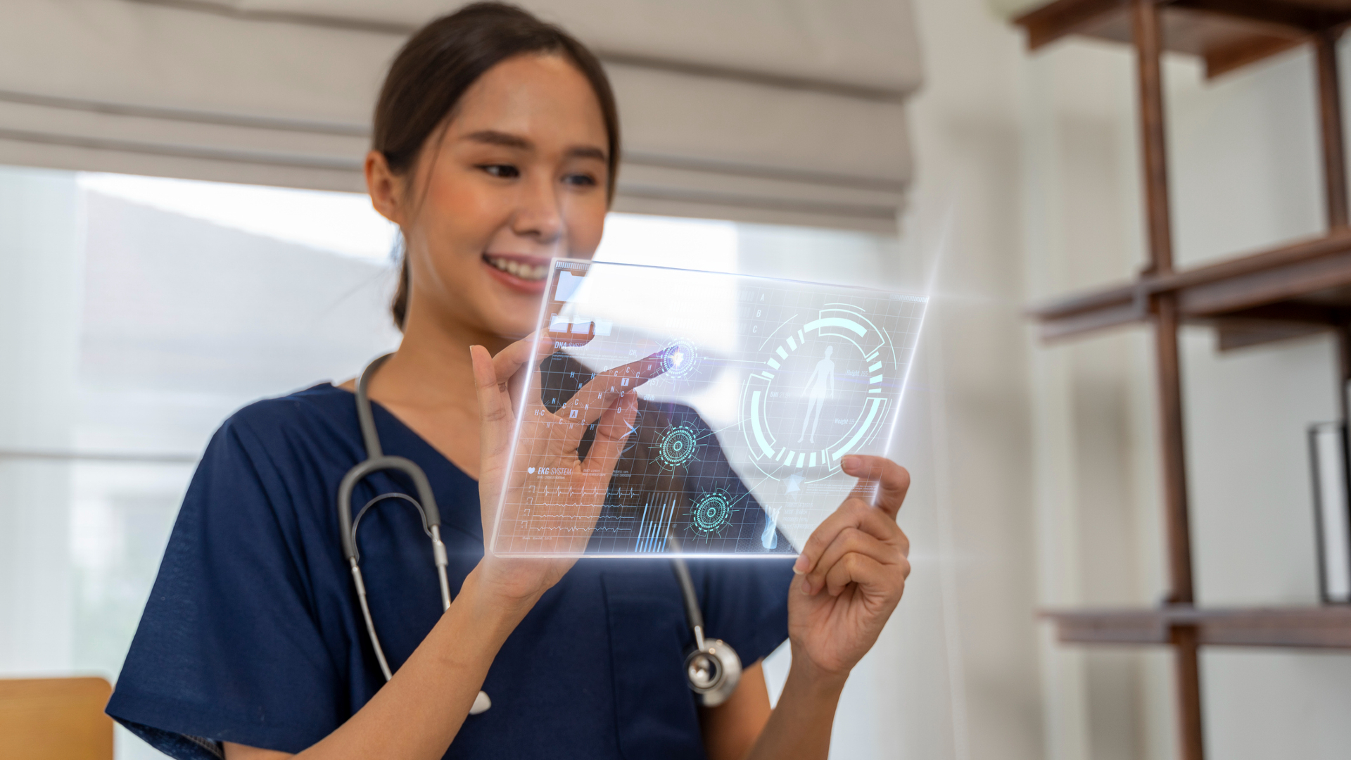 A woman with dark straight hair pulled back wearing navy blue scrubs and a stethascope taps on a glass panel lit up with various technological images