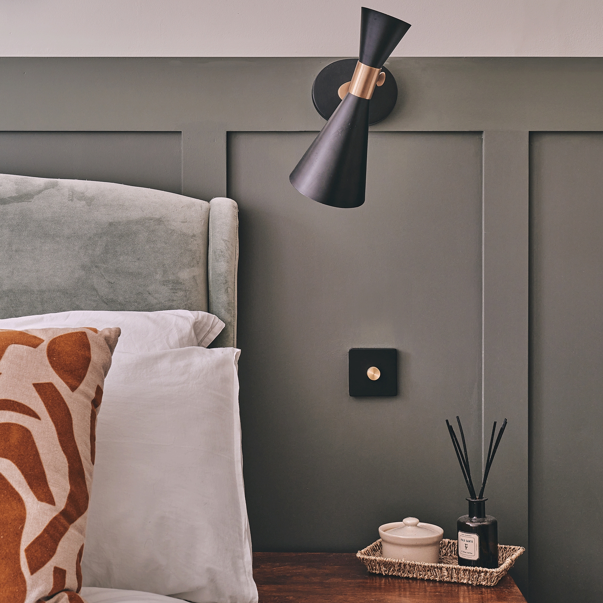 a bedroom with dark green wall panelling bedside wall lights and patterned cushions