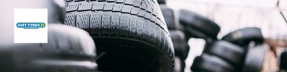 Just Tyres logo placed over a wide image of tyres piled up 