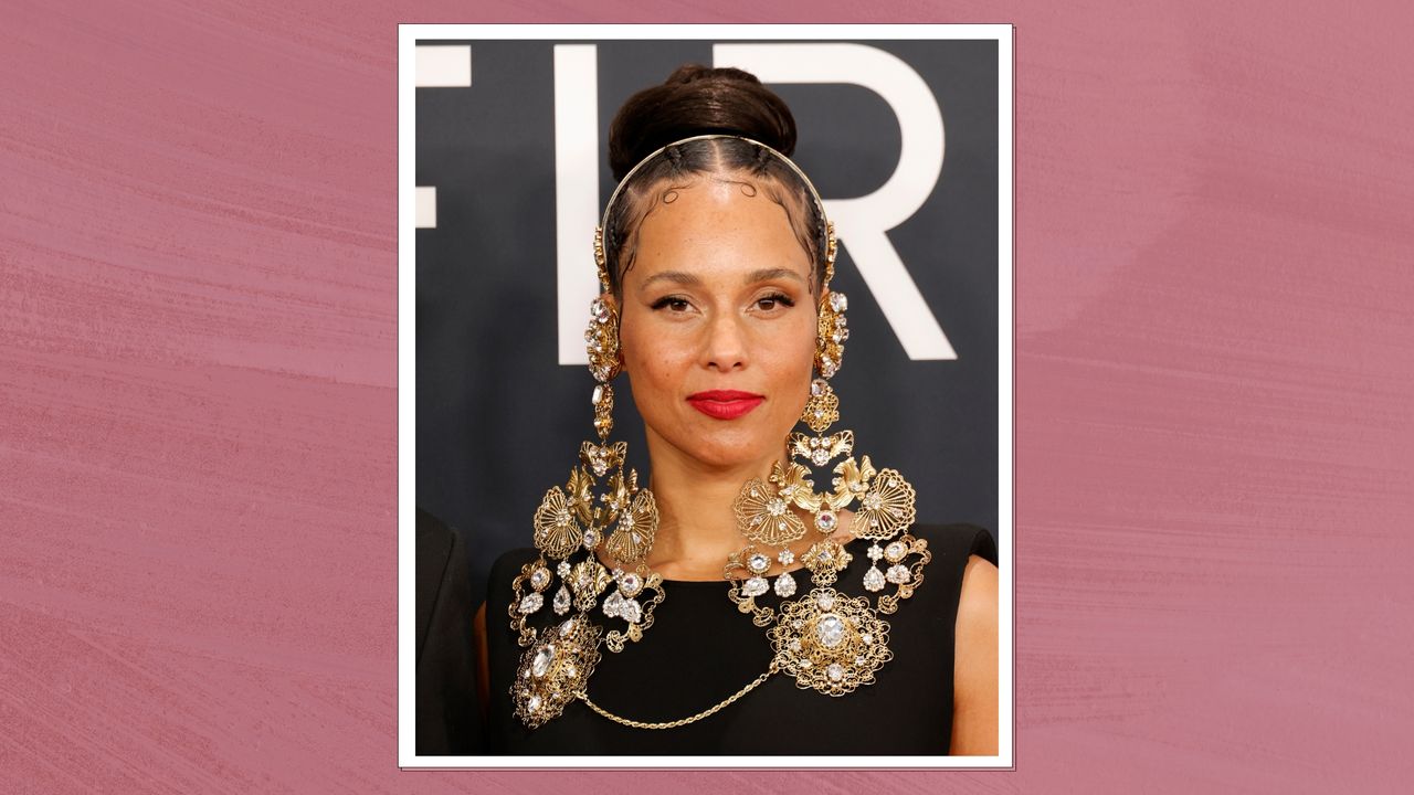 Image of Alicia Keys with brunette hair braided into a bun, wearing minimal makeup and bright red lipstick, on a deep mauve background