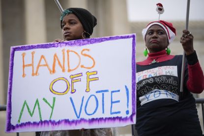 A photograph of voting rights activists outside the U.S. Supreme Court holding a sign saying "Hands Off My Vote!"