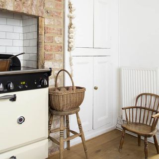 kitchen area with white wall and cabinet with brick chimney breast and wooden basket with chair.