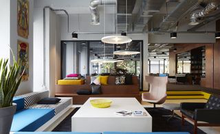 The Student Hotel lounge with exposed ducting in ceiling, bench seating, blue and grey striped cushions and white marble table