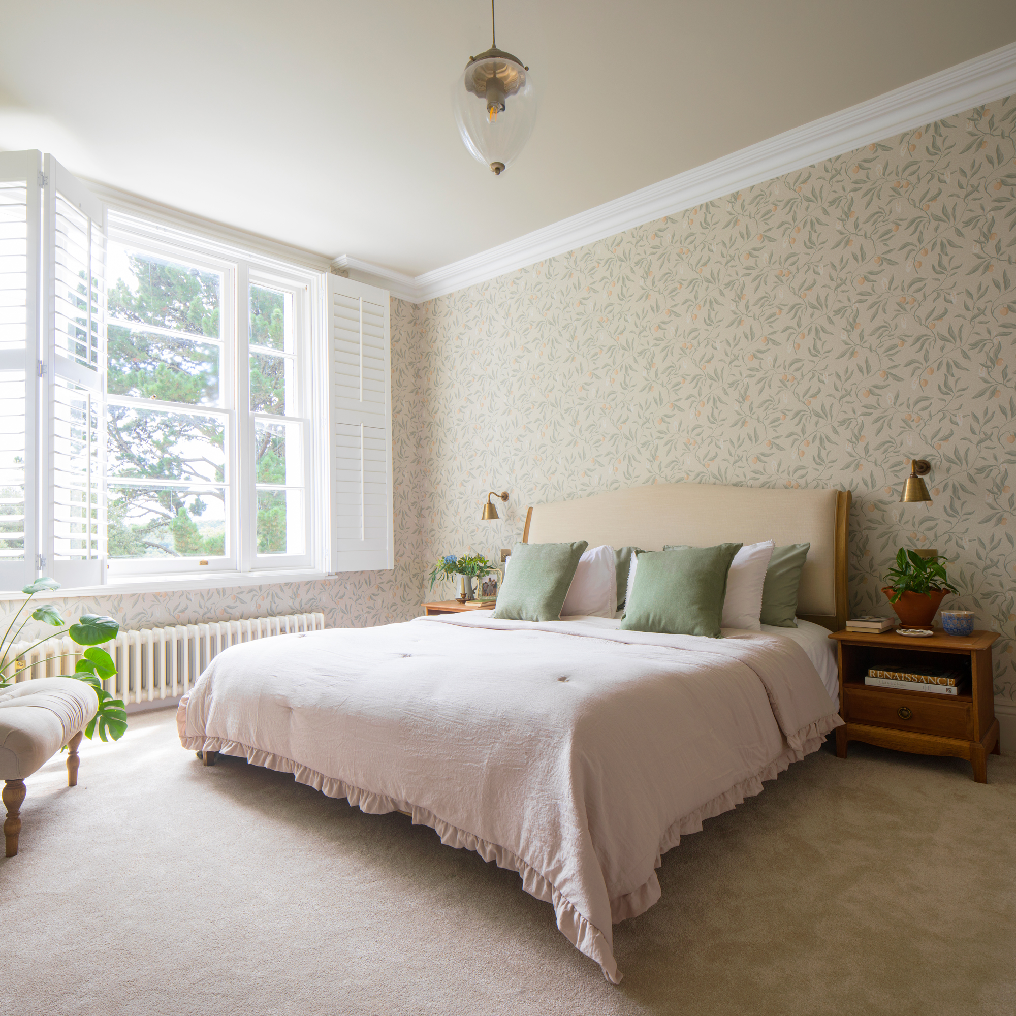 a bedroom with botanical wallpaper on the walls, and a window with shutters