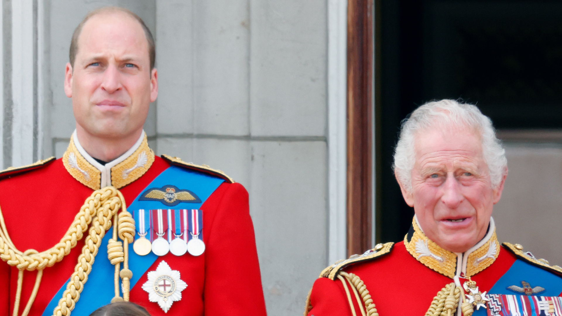 Prince William and King Charles wear red military uniforms as they stand on the Buckingham Palace balcony