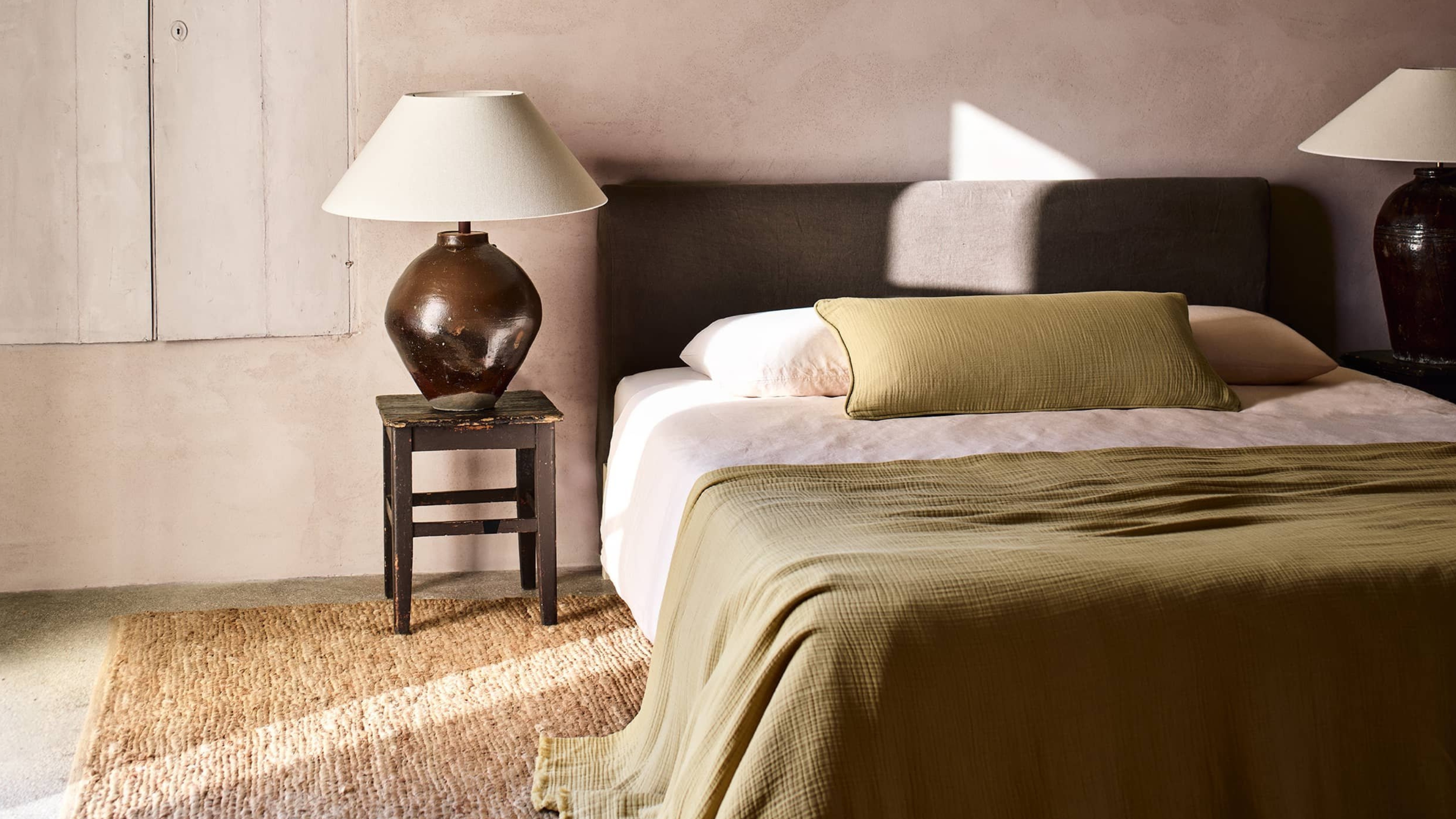 a bedroom with limewash wall, with textural bedding on a fabric bed, and large lamps on nightstands