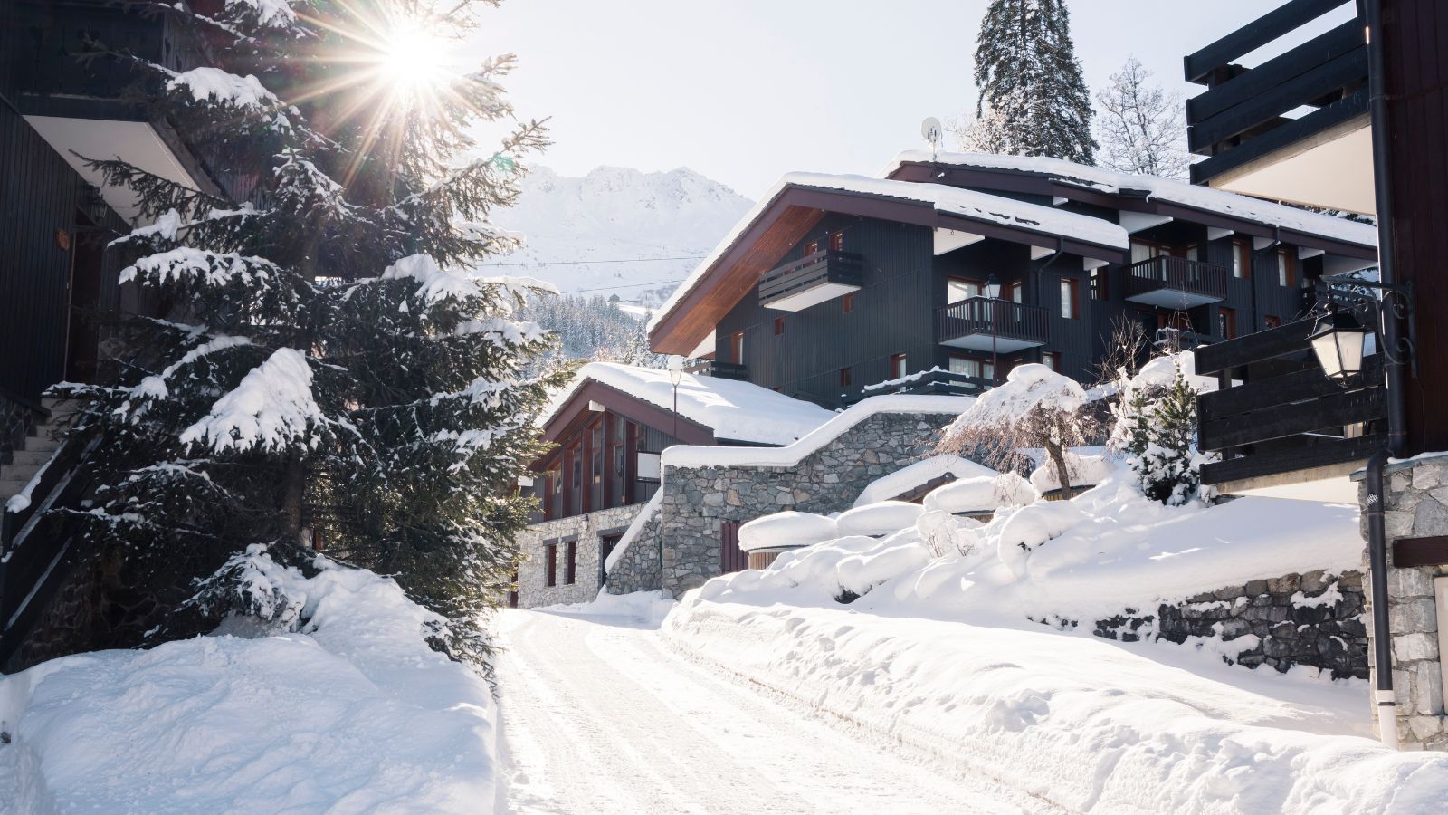 A large luxury home up a steeped driveway, covered in snow. Mountains in the background. 