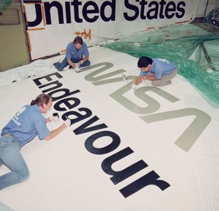 three people holding brushes and painting nasa endeavour on the shuttle.