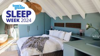A bed is placed in a blue bedrrom under exposed beams and a sloping ceiling
