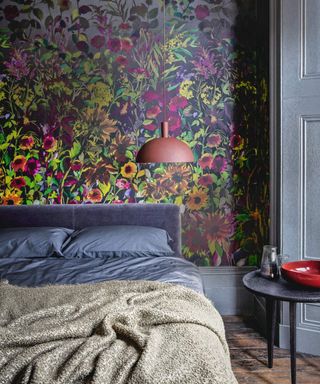 Bedroom with dramatic floral wallpaper behind the headboard of the double bed, with wooden flooring and grey paintwork.