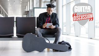 A man waits at an airport gate, with his guitar in its case at his feet