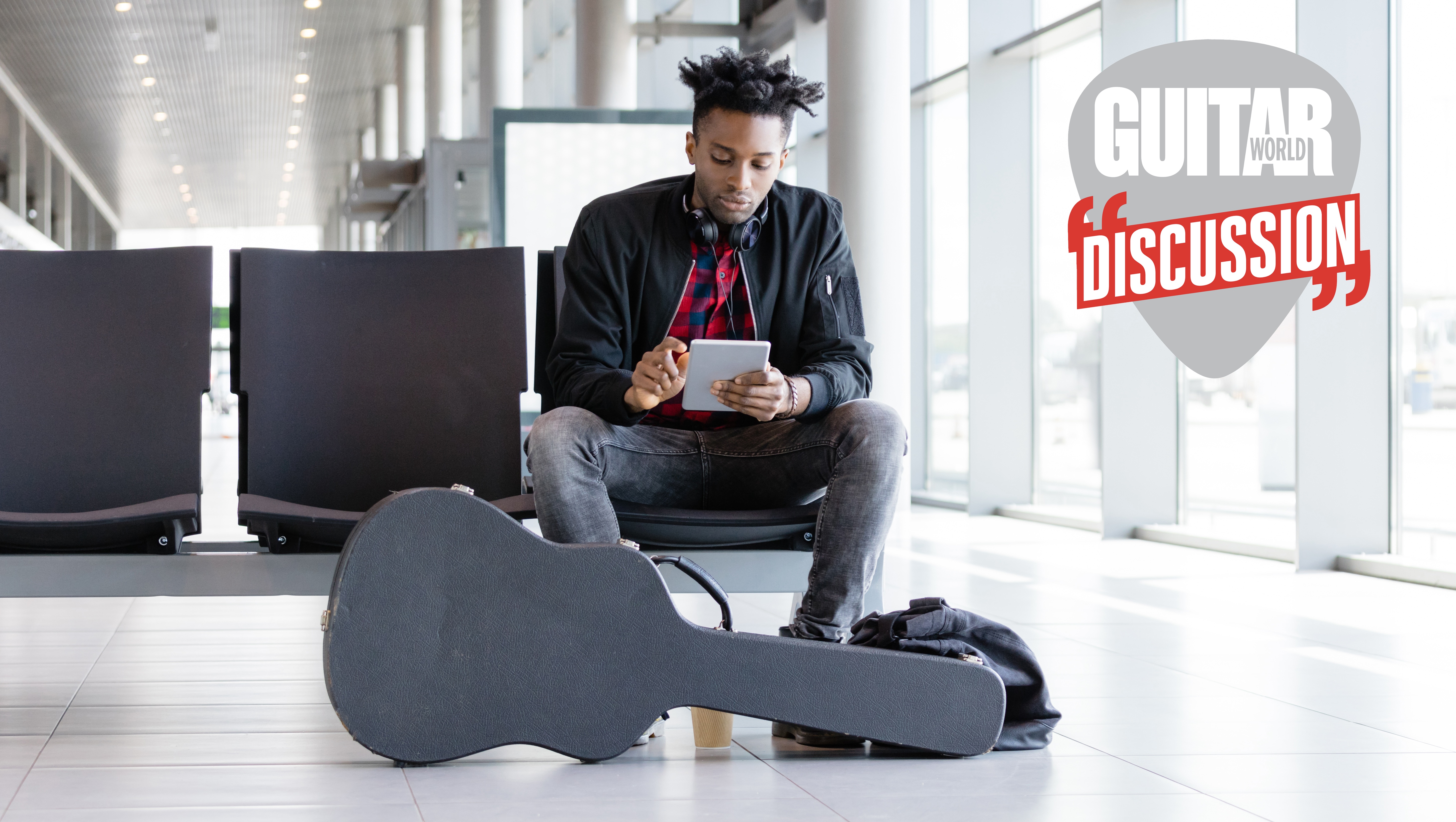 A man waits at an airport gate, with his guitar in its case at his feet