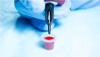 A person holding a tattoo needles with a pot of red ink.