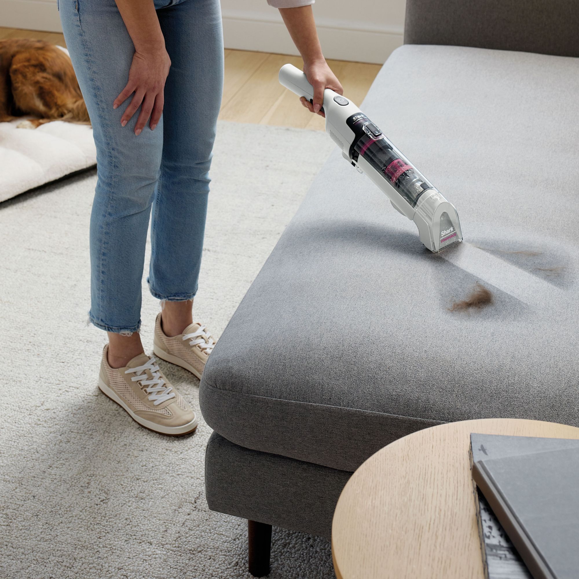 Woman using the Shark Stainforce Spot Cleaner HX100UKT on a grey footstool with a stain and pet hair on it