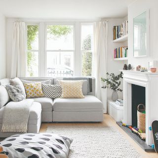 A white living room with a light grey corner sofa and fireplace matching the colour of the walls