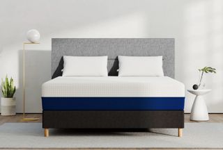 Image shows an Amerisleep memory foam mattress placed on a grey fabric bedframe sat against a white wall