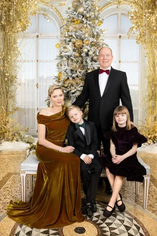 Princess Charlene wearing a gold velvet gown, Prince Jacques and Prince Albert wearing tuxedos and Princess Gabriella in a velvet dress posing in front of a gold Christmas tree