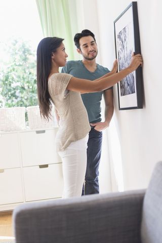 A couple hanging a picture on the wall of their home