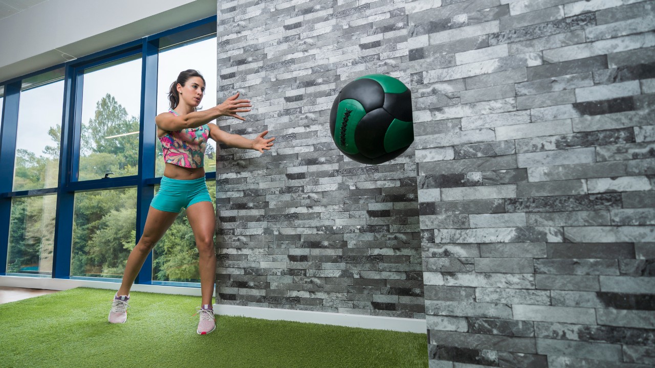 Une femme lance un médecine-ball contre un mur
