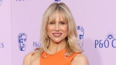 Image of Lucy Punch smiling with blonde shoulder-length hair with fringe and wearing an orange dress