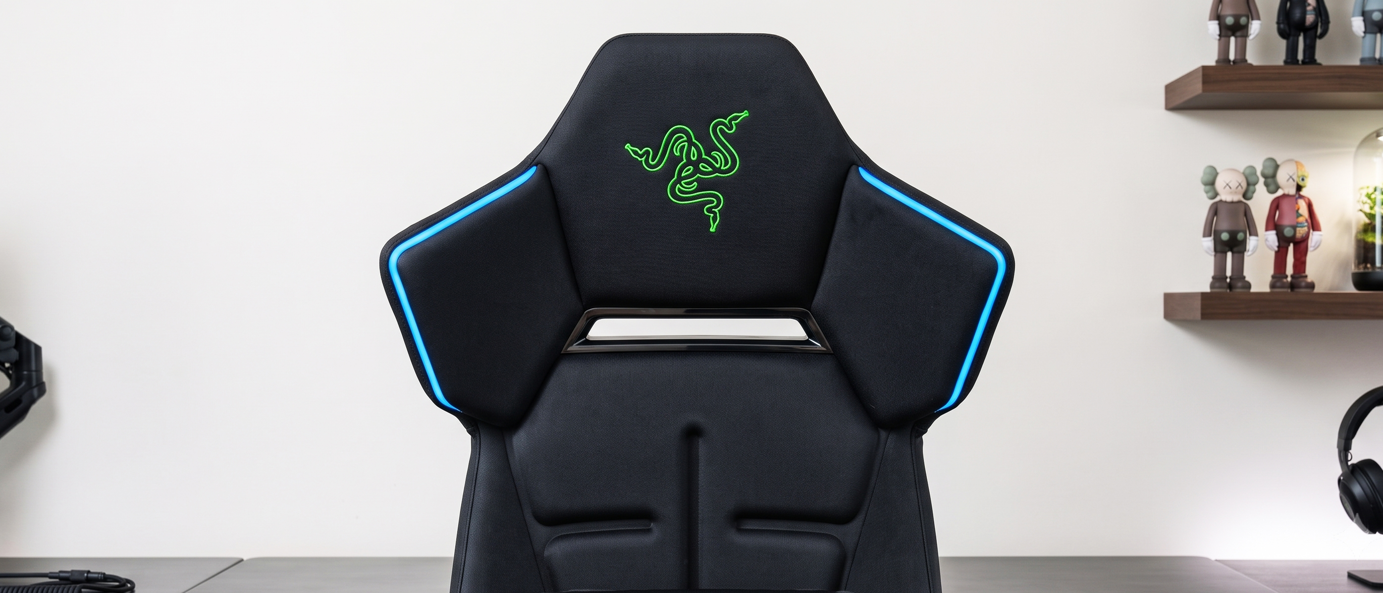 A close-up view of the Razer Soma Chroma gaming chair, showing the glowing green Razer logo and blue LED light strips.