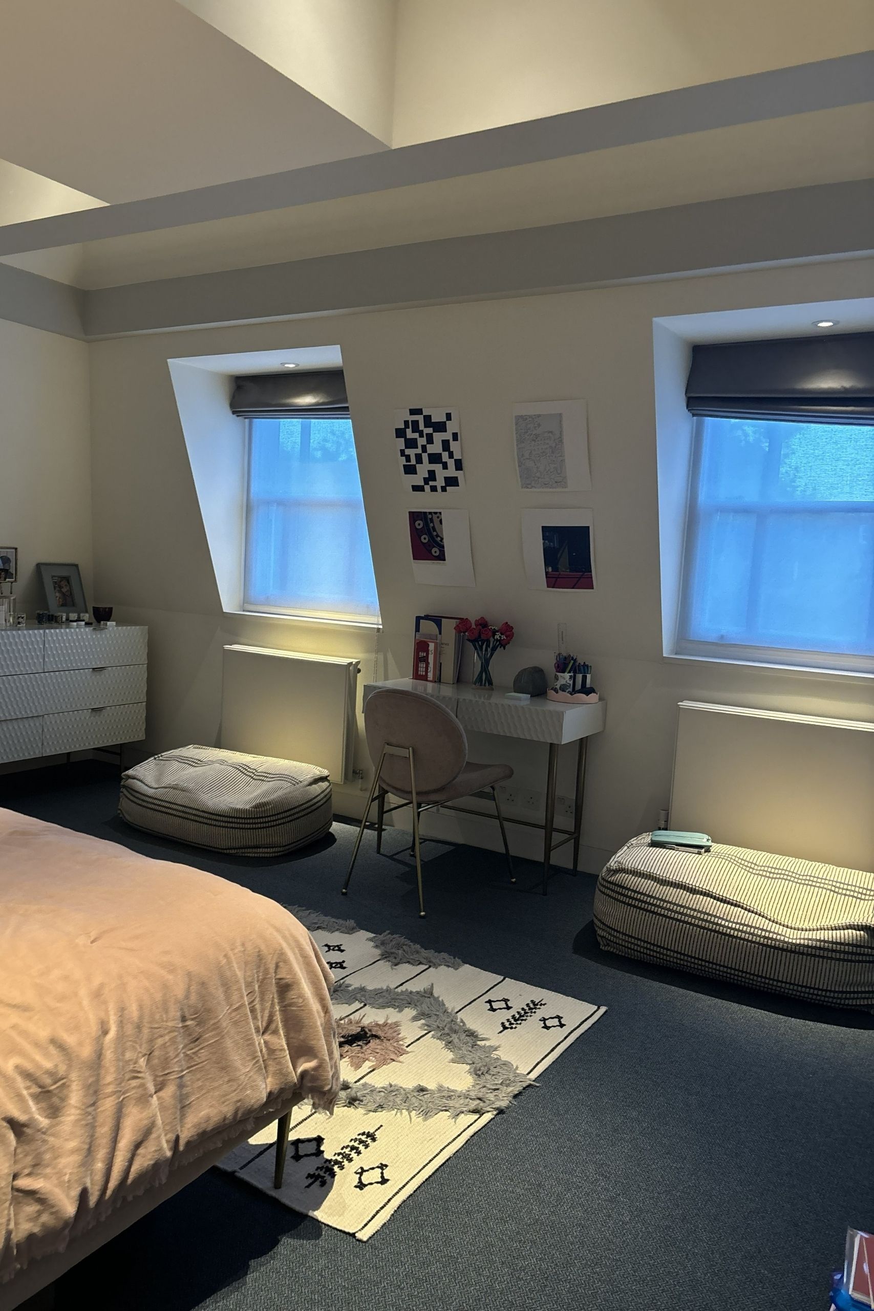 Image of the desk area of a bedroom suite with two windows on either side with bean bags underneath them. The carpets are navy and the walls are white.