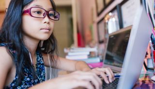 Child typing on a laptop - digital technology can drive social impact in education 