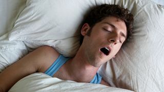 A man sleeping on his back with his mouth open snoring