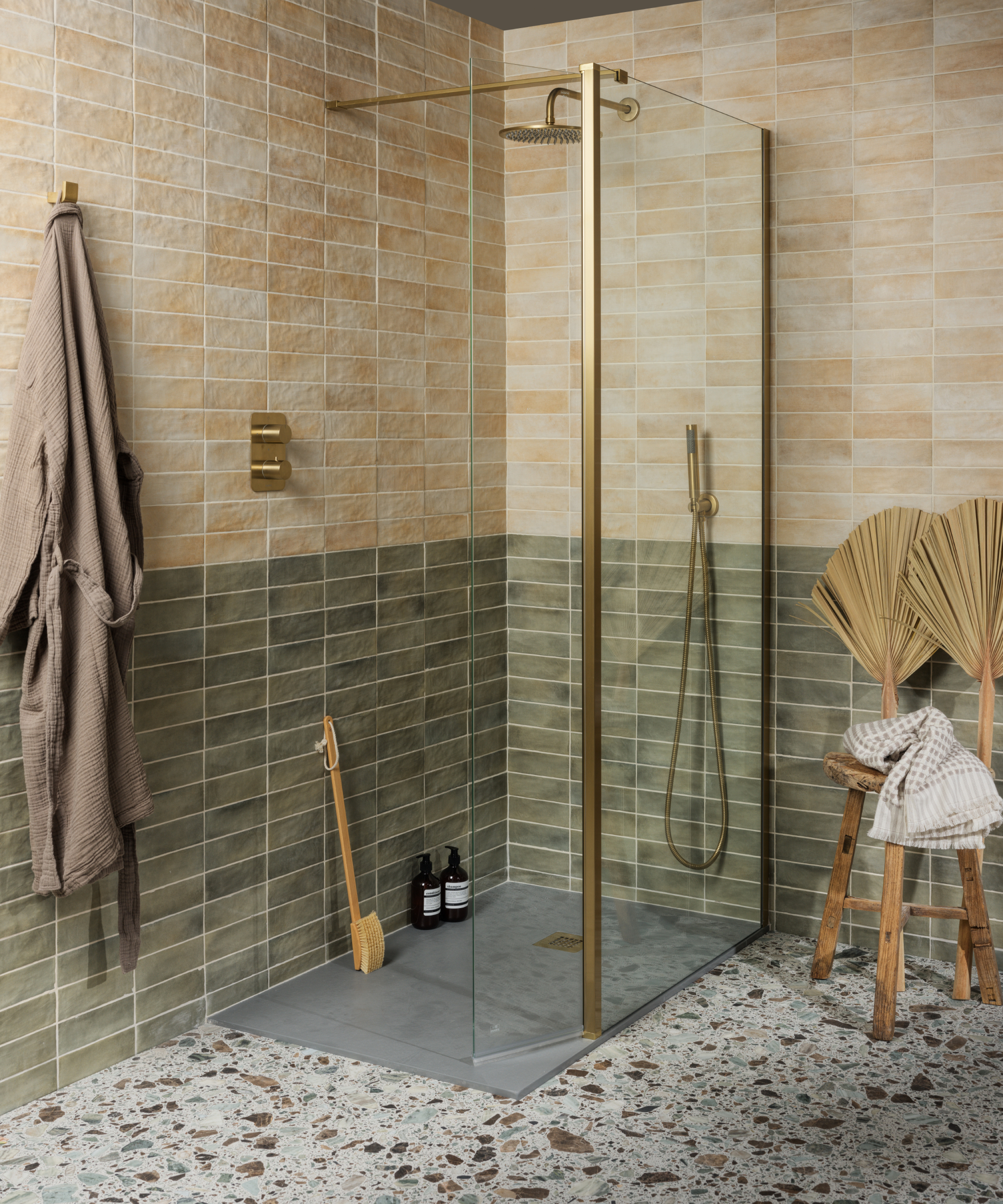 bathroom with glass and brass shower enclosure, terrazzo floor tiles, green and pale terracotta and cream wall tiles